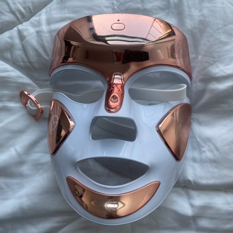 The Dr. Dennis Gross DRx Spectralite Faceware Pro mask laying face up on a white comforter.