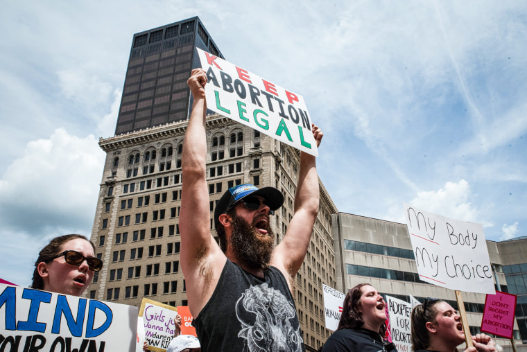 Protesters hold signs at a protest, main sign reads "Keep Abortion Legal"