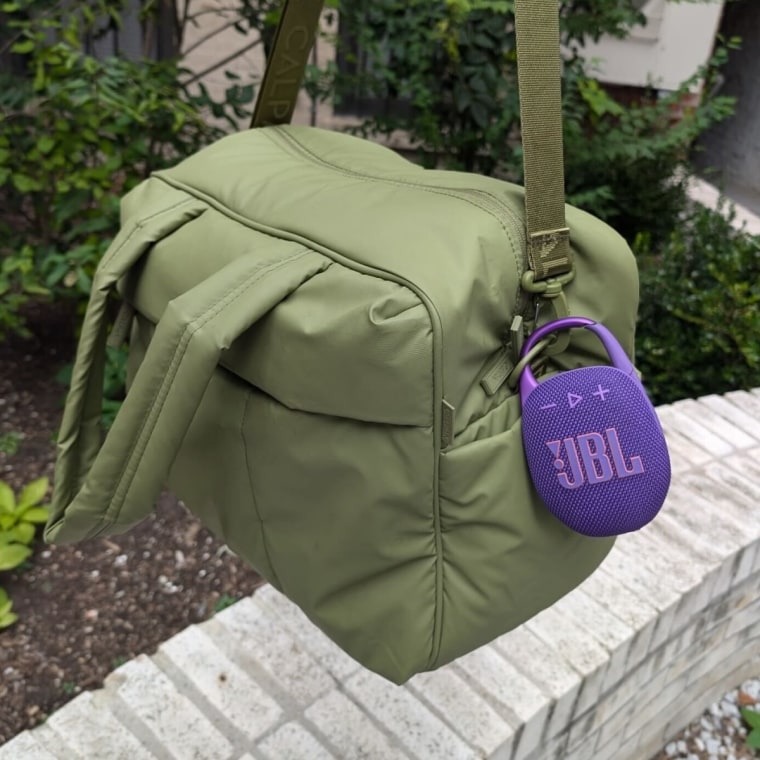 Purple oval-shaped JBL speaker clipped onto green duffel bag.