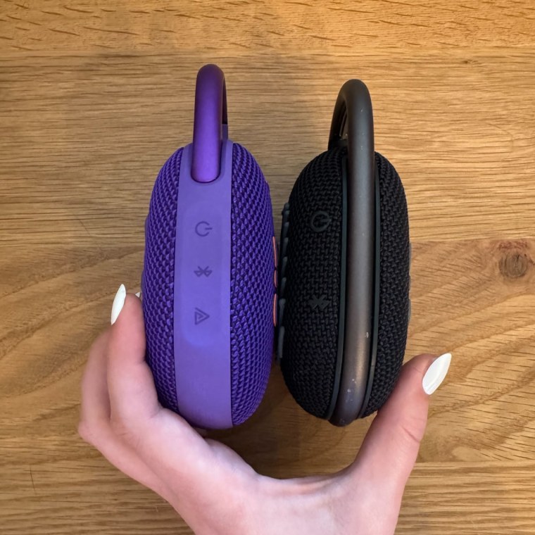 On the right, a purple oval-shaped JBL speaker has buttons for power, Bluetooth, and Auracast. To the left, a black oval-shaped JBL speaker has buttons for power and Bluetooth.