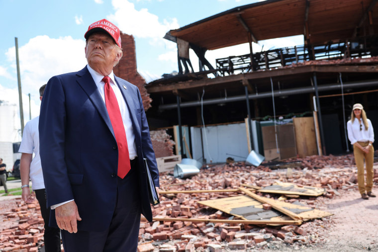 Donald Trump looks around at a debris filled building and street outside