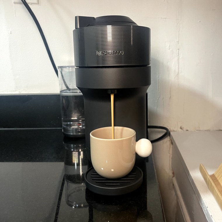 The black Nespresso Vertuo Pop+ brews an espresso into a beige espresso mug.