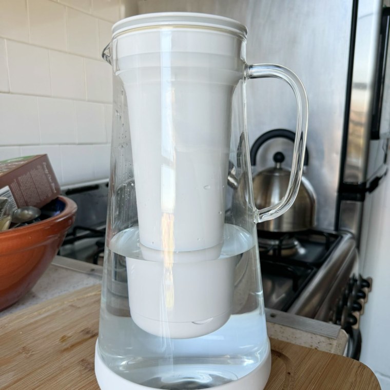 The Lifestraw Water Pitcher on a wooden cutting board, in front of a gas stovetop with a tea kettle on it.