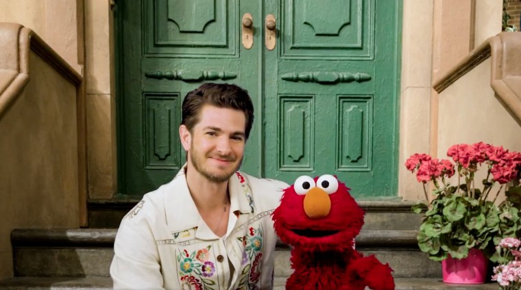 Andrew Garfield and Elmo sit on a stoop