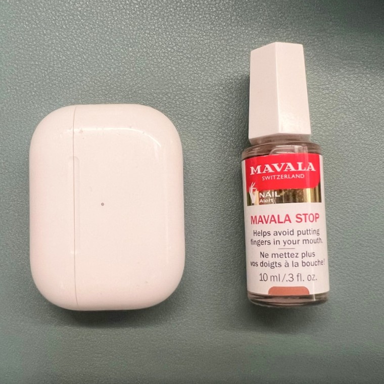 Mavala no-bite polish on a green background next to an AirPods Pro case.