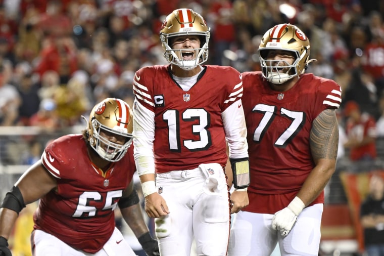 San Francisco 49ers quarterback Brock Purdy celebrates with guards Aaron Banks and Dominick Puni after scoring a touchdown against the Dallas Cowboys.