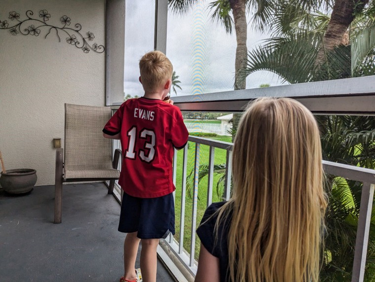 Two children look beyond the fence of a porch on a cloudy day