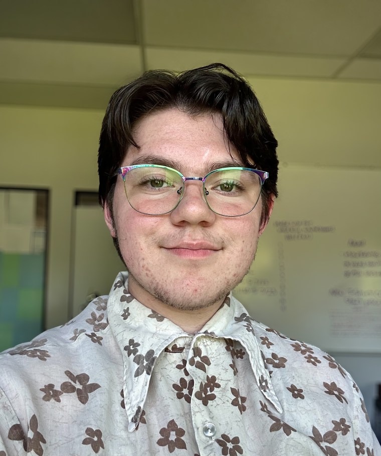 Selfie of a person in glasses in a classroom; whiteboard in the background