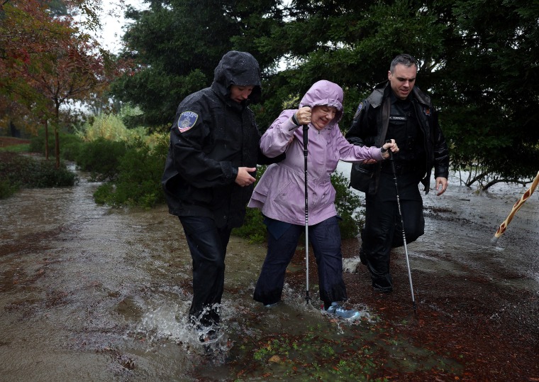 Police officers help an elderly woman walk in floodwater